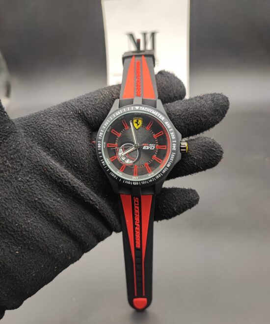 Scuderia Ferrari Red Rev Evo style men's sports watch featuring a matte black case, black honeycomb dial with red index hour markers, yellow racing shield emblem at 12 o'clock, and a red-striped black silicone strap held in a black gloved hand.