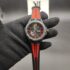 Scuderia Ferrari Red Rev Evo style men's sports watch featuring a matte black case, black honeycomb dial with red index hour markers, yellow racing shield emblem at 12 o'clock, and a red-striped black silicone strap held in a black gloved hand.
