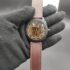 : Fossil style men's automatic skeleton watch featuring a black knurled textured bezel, exposed gold-tone mechanical movement, and a smooth brown leather strap with contrast stitching held in a black gloved hand.