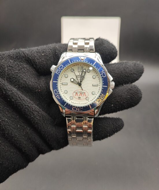 Omega Seamaster style automatic dive watch with a white wave textured dial, blue ceramic bezel, and stainless steel bracelet held in a black gloved hand.