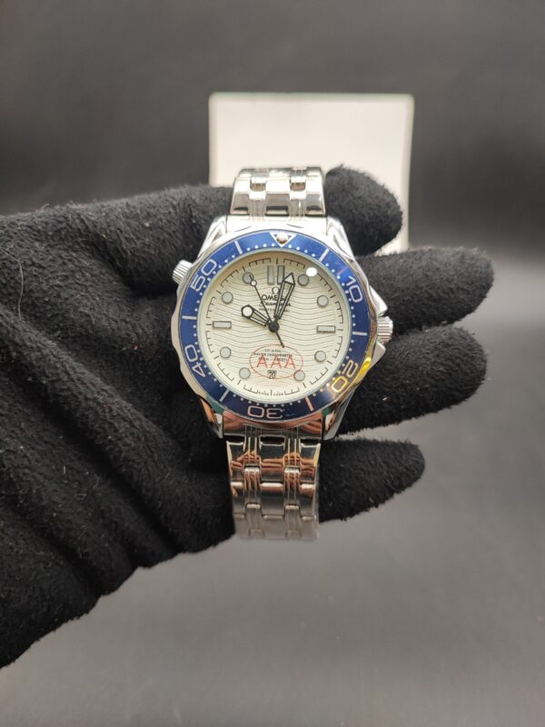 Omega Seamaster style automatic dive watch with a white wave textured dial, blue ceramic bezel, and stainless steel bracelet held in a black gloved hand.