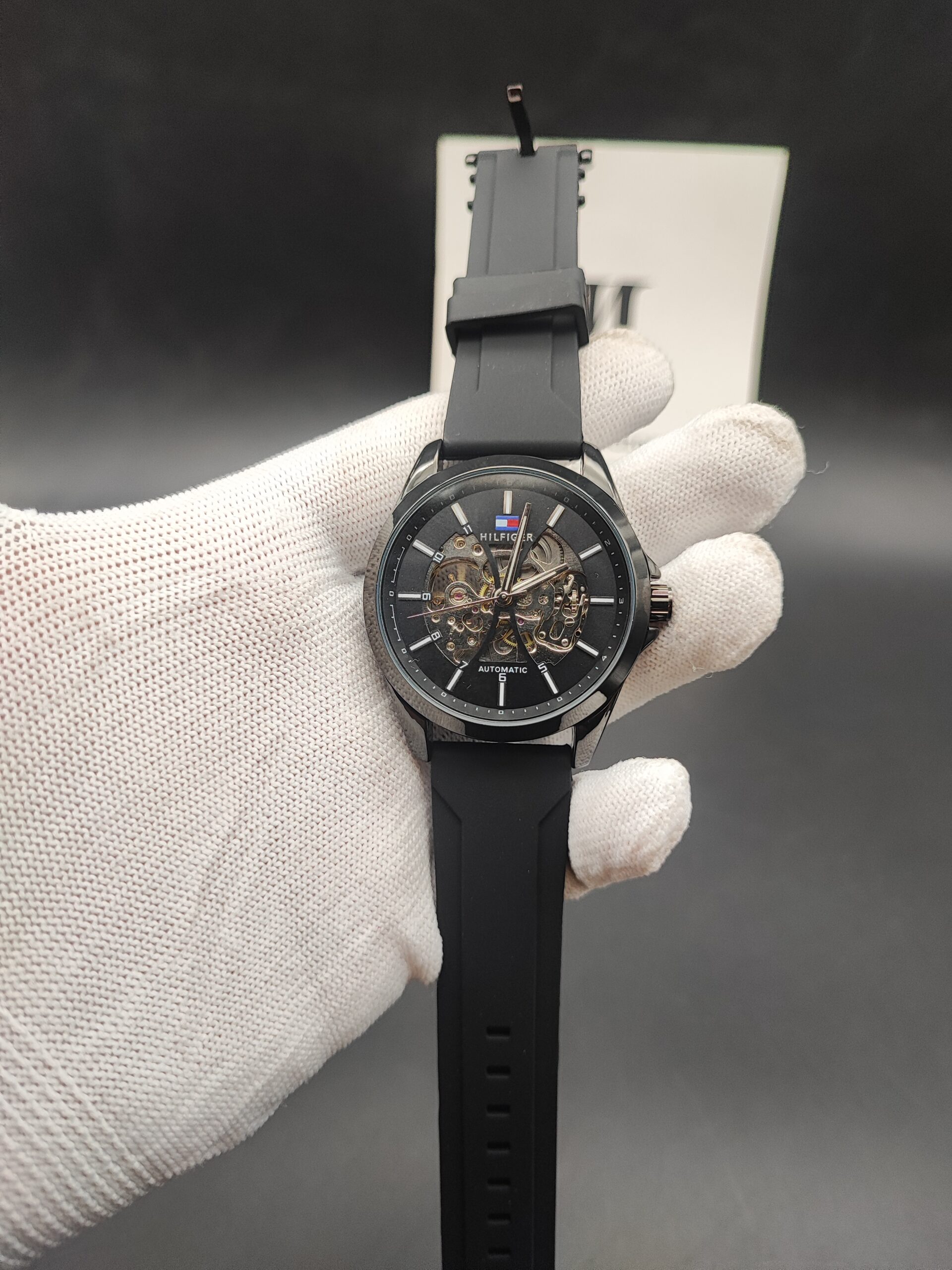 Tommy Hilfiger style men's automatic skeleton watch featuring a polished black case, a matching black outer dial ring, an exposed mechanical core,
