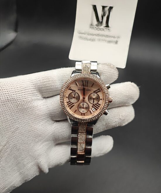 ichael Kors style women's dual-tone chronograph watch featuring a crystal-studded rhinestone bezel, rose gold sunray dial with Roman numerals, and a silver bracelet with diamond-encrusted center links held in a white gloved hand.