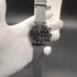 Emporio Armani style men's watch featuring a gunmetal grey case, a black horizontal-paved dial with triple subdials, a silver eagle logo at 12 o'clock, and a textured grey rubber strap with embossed lettering held in a white gloved hand.